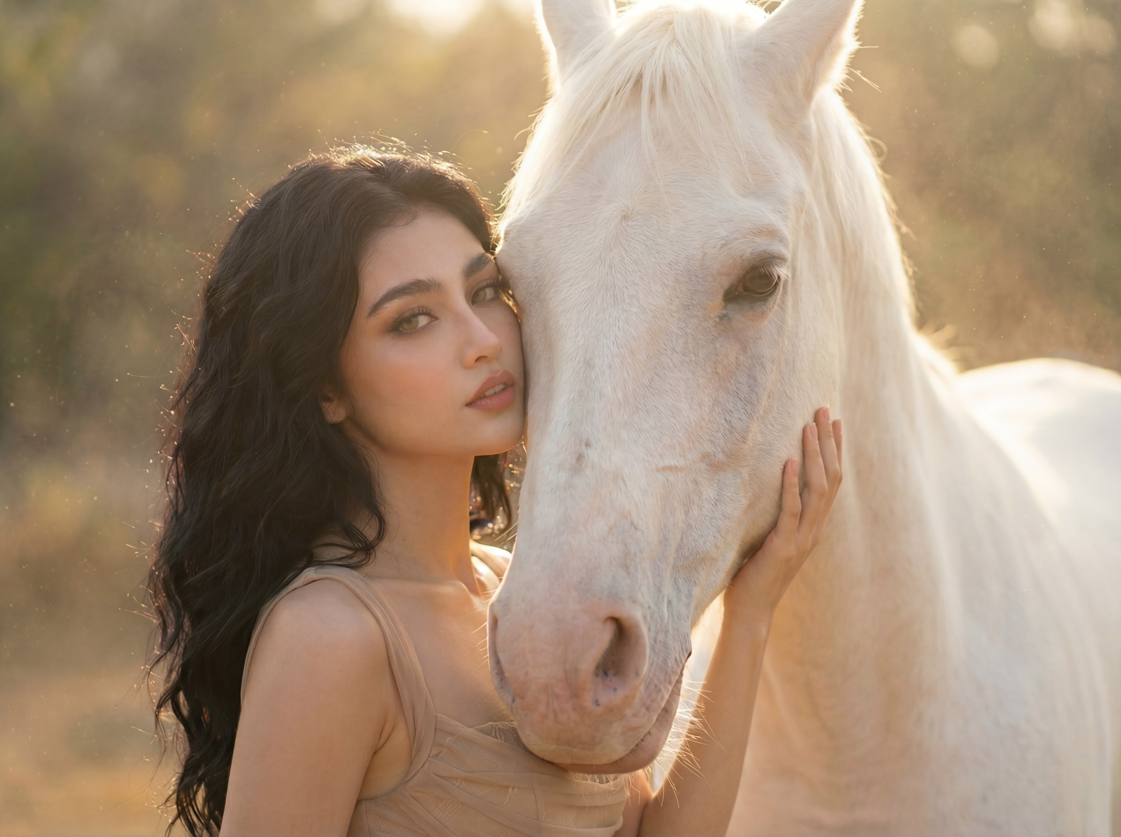 Elegant outdoor portrait of a woman with long dark wavy hair posing beside a white horse in warm golden sunlight. She wears soft glam makeup featuring CoreLash wispy lashes and natural beauty styling, creating a serene and dreamy aesthetic.